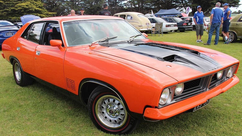A classic vibrant orange Ford Falcon XB GT four-door sedan parked on green grass at an outdoor car show.