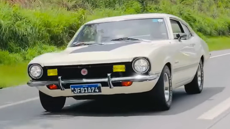 An off-white Brazilian Ford Maverick GT fastback coupe driving down a two-lane asphalt highway.