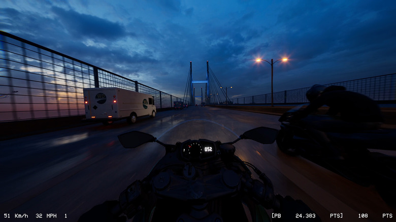 A rider on a motorcycle, next to another, riding towards a bridge on a wet highway at night