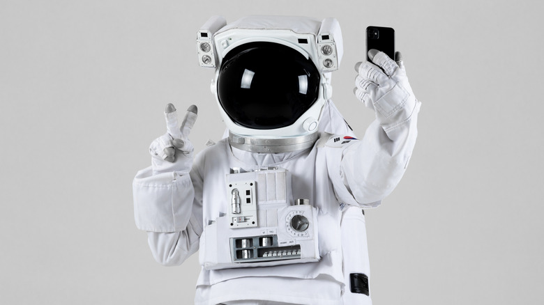 An astronaut in full space suit flashes a peace sign for a selfie