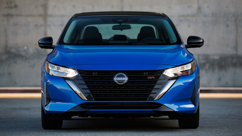 A head-on shot of a blue 2025 Nissan Sentra SR with a black roof parked in front of a concrete wall