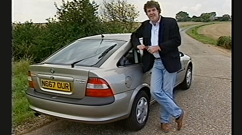 screenshot showing a young Jeremy Clarkson leaning on a silver Vauxhall Vectra in front of a tree