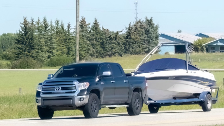A black Toyota pickup towing boat on a road