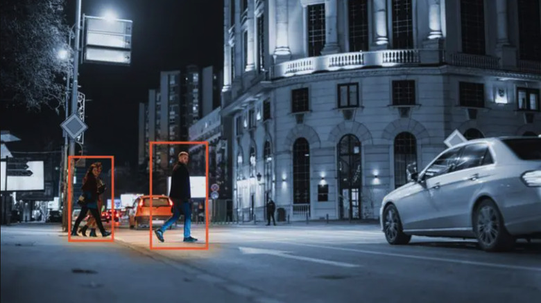 A black and white photo of a sedan approaching a crosswalk, and three humans are highlighted by orange rectangles and lit by the ISS AI Softlit software.