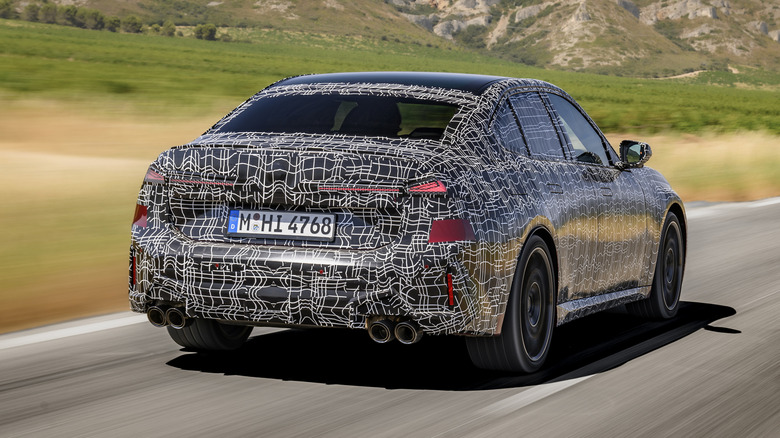 Rear 3/4 view of the camouflaged 2027 BMW M350 xDrive in motion.