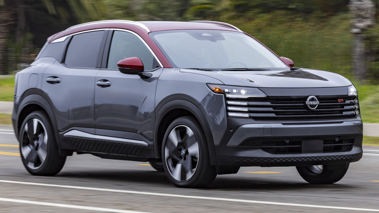 2026 Nissan Kicks driving on a road with trees and various plants in the background