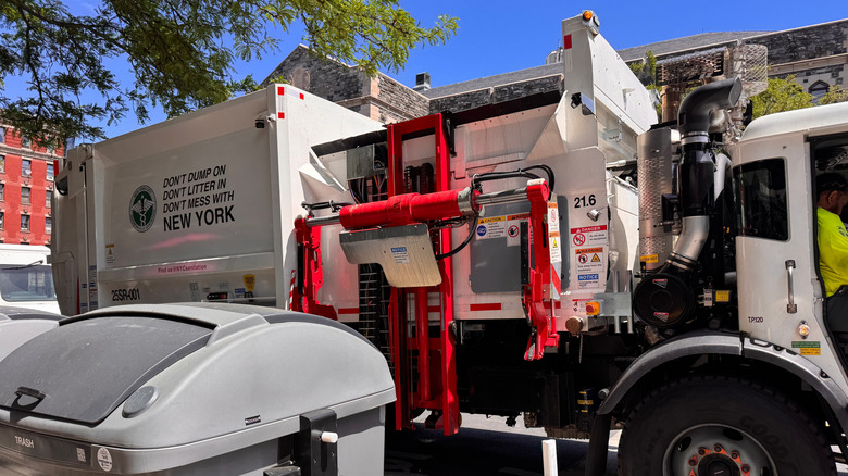 New York, NY USA - May 20, 2025 : New York City side loading garbage truck next to new large curbside Empire Bin for trash collection in West Harlem, NYC