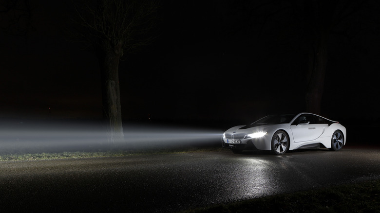 A white BMW i8 parked on asphalt at night with its headlights on showing how powerful its laser headlights are