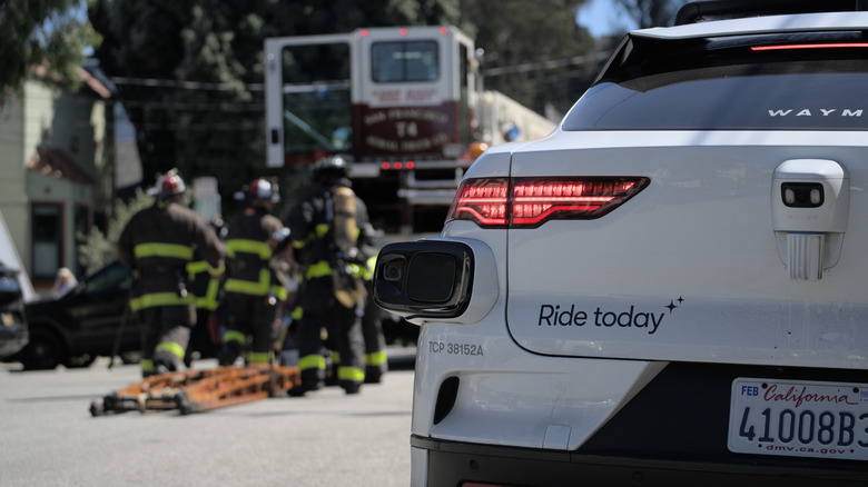 A Waymo car approaches the scene of an emergency while firefighters respond.