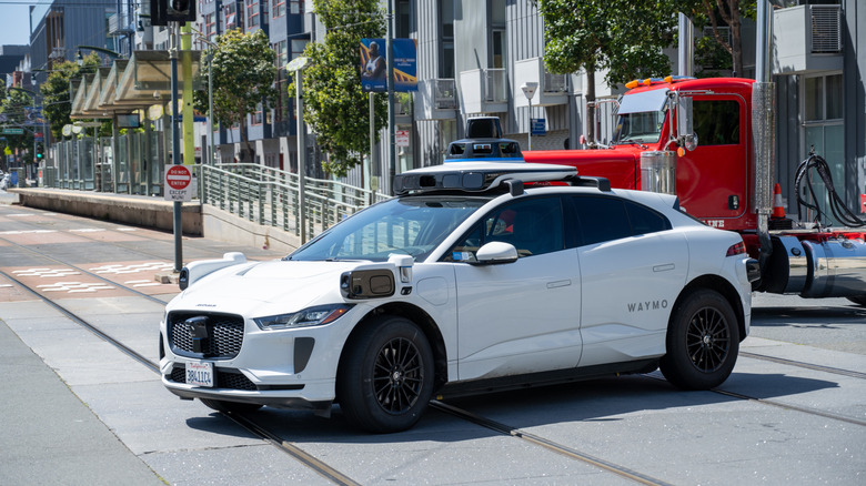 A white Jaguar I-Pace Waymo crosses light rail tracks in San Francisco.