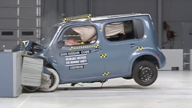 A screenshot from the IIHS moderate overlap crash test of a light blue 2009 Nissan Cube the moment it hits the barrier