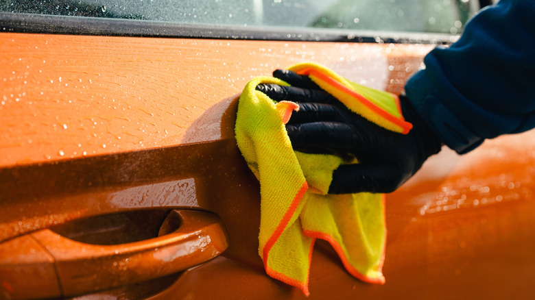 Man wearing gloves wiping a car with a yellow microfiber towel