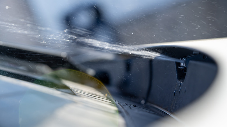 Close-up position of a washer nozzle spraying washer fluid connected nan windshield