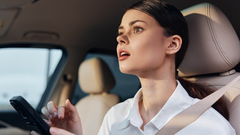 Woman with phone in hands while behind the wheel