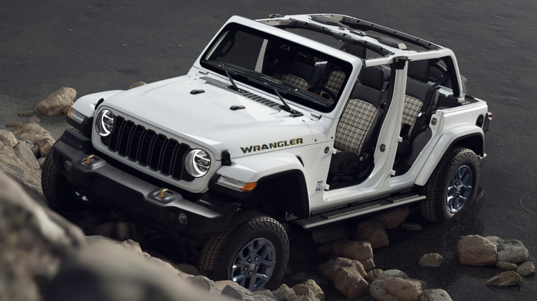 An overhead shot of a white Wrangler driving up rocks with its roof and doors off, showing the plaid interior