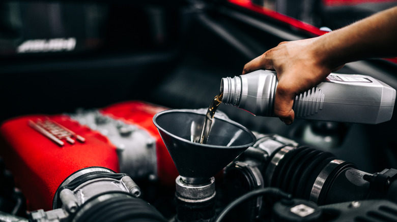 A hand pours a quart of oil into a funnel directed into a Ferrari engine.