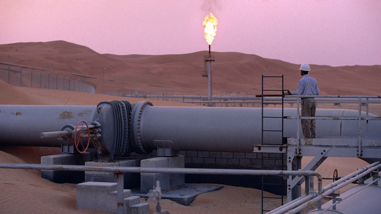 A worker stands at a pipeline, watching a flare stack at the Saudi Aramco oil field complex facilities at Shaybah in the Rub' al Khali ("empty quarter") desert on March 2003 in Shaybah, Saudi Arabia.