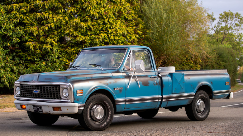 A Blue Patina Chevy C20 driving on the street with trees in the background