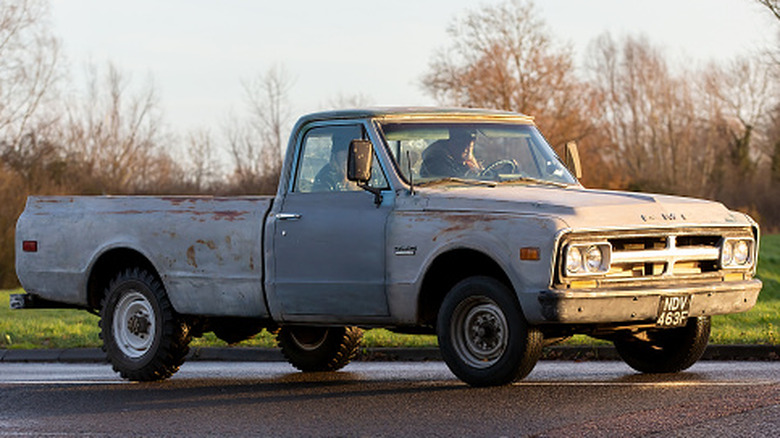 A late-1960s GMC C/K pickup truck on a roadway with trees and grass in the background
