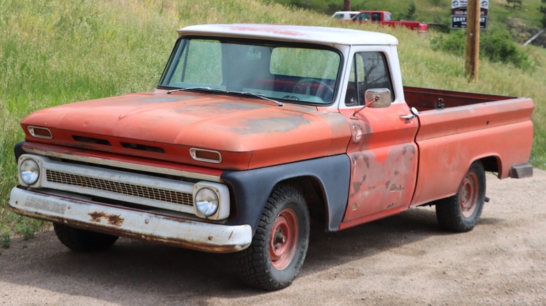 A 1963 Chevy C10 pickup truck with faded red paint parked on a country road