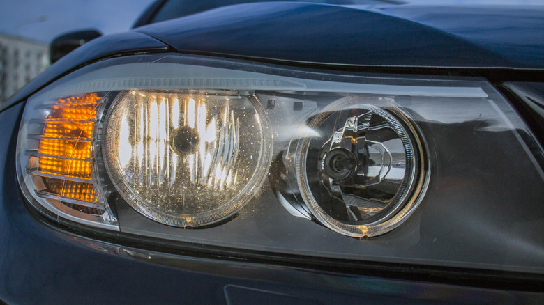 A close-up of a BMW 3-Series with illuminated headlights and turn signal.