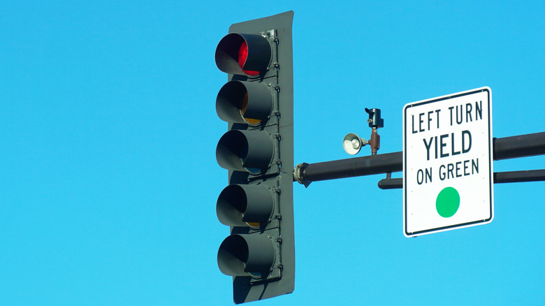 Red traffic light with a left-turn yield on green sign against a clear blue sky.