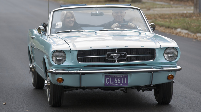 A man and woman driving in a blue 1964 Mustang Convertible