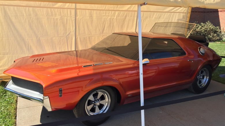 A red-orange 1966 AMC AMX prototype showing the rear trunk lid opened for the Rumble Seat