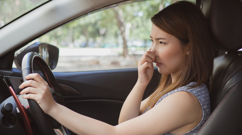 A woman behind the wheel of a car holding her nose.