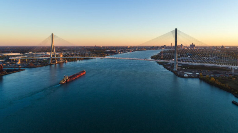 The Gordie Howe International Bridge across the Detroit river near sunset as a freighter passes beneath.