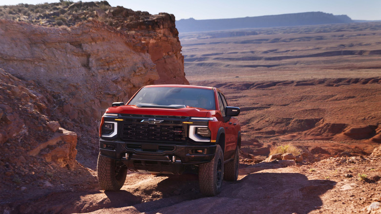 A Red 2027 Chevrolet Silverado climbing a rocky mountain-like terrain in the desert.