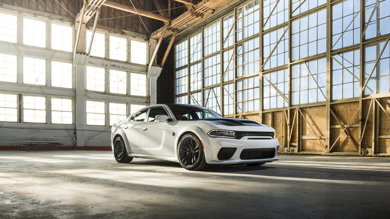 A white Dodge Charger SRT Hellcat Redeye with a matte black hood, in an abandoned garage warehouse building with lots of windows.