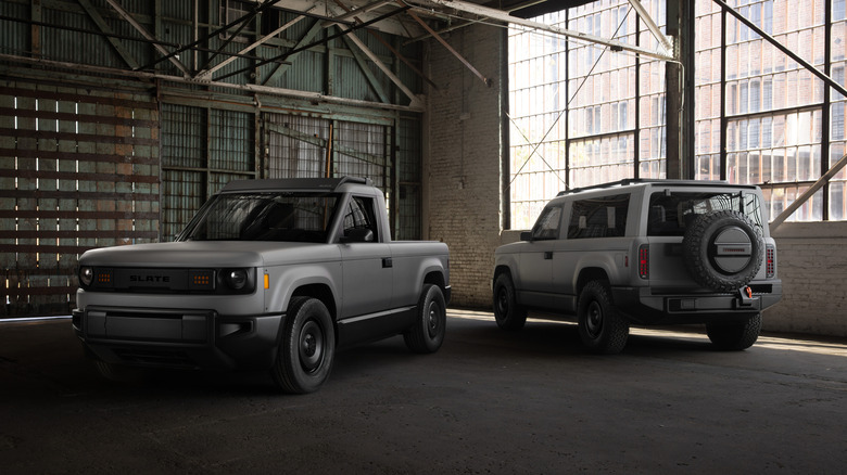 A grey Slate truck with black cap wheels and a grey slate truck with the cab cover and tire cover on the hatch, set inside an abandoned warehouse.