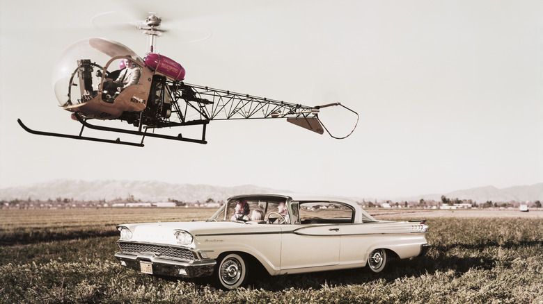A Mercury Monterey with a Bell helicopter hovering above