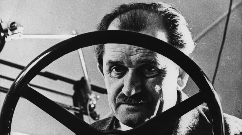 Ferdinand Porsche stares through the spokes of a steering wheel