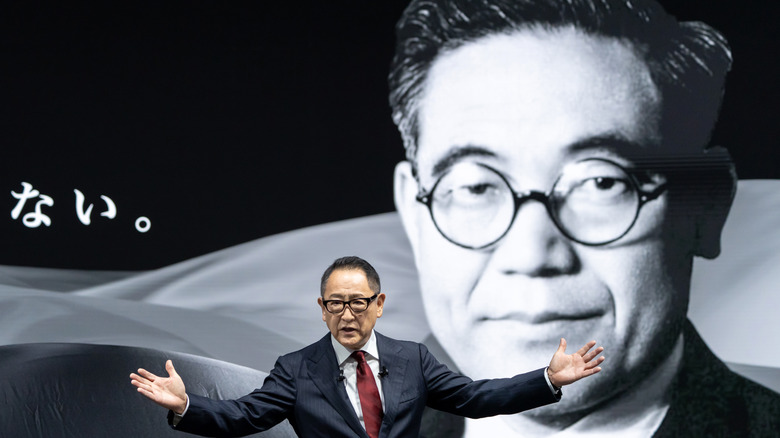 Akio Toyoda stands on stage in front of an image of Kiichiro Toyoda