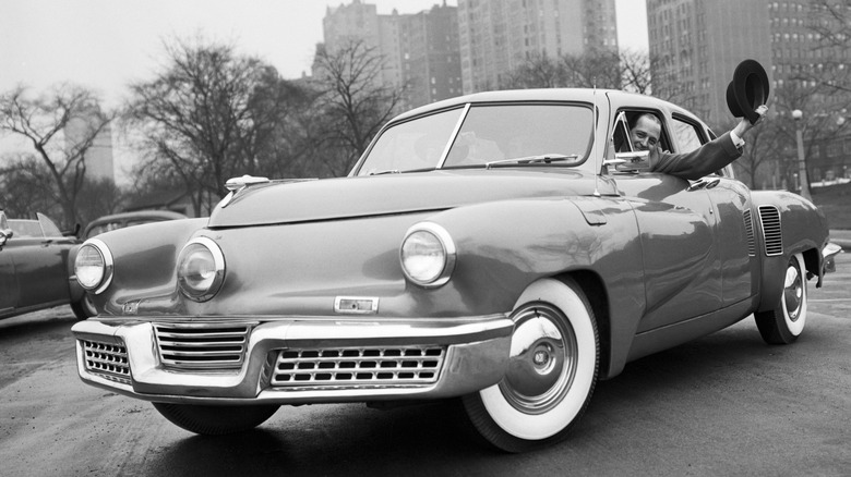 Automotive designer Preston Tucker celebrates being aquitted of charges of fraud over the failure of his automobile business. He is seen waving from one of the few Tucker automobiles produced.