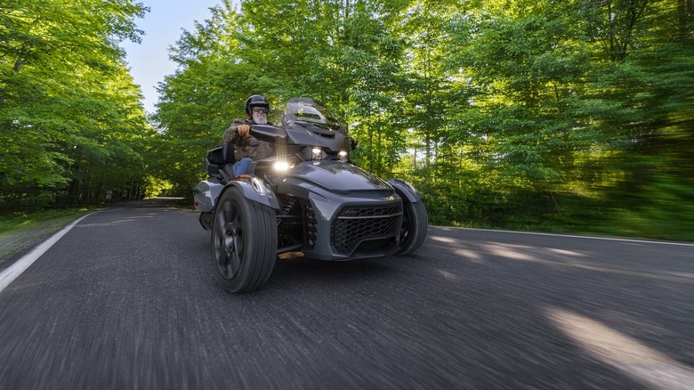Front 3/4 view of a gray 2027 Can-Am Spyder on a forest road
