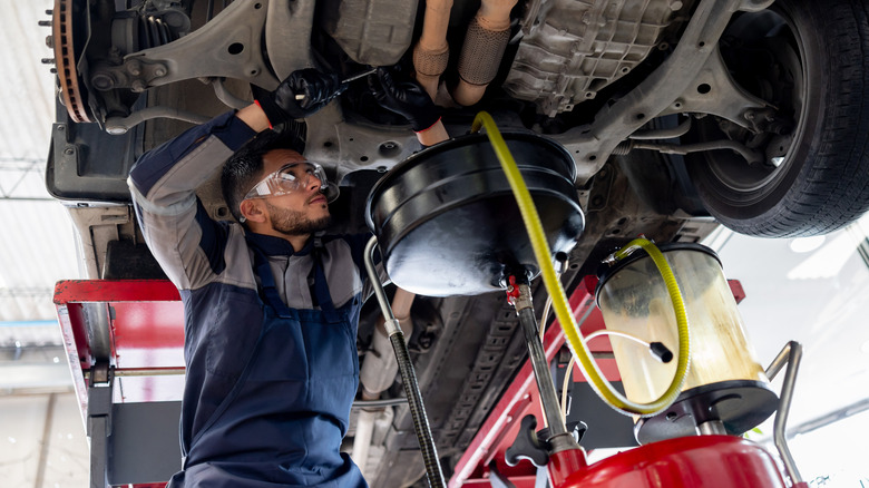 A man draining lipid from underneath a car.
