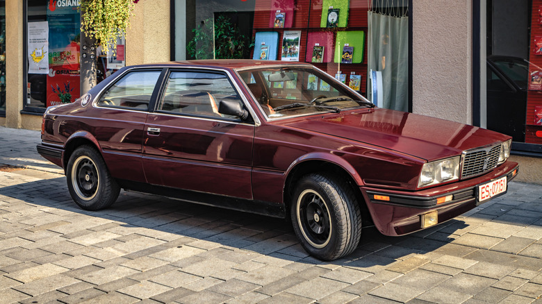 A burgundy Maserati Biturbo outside a shop.