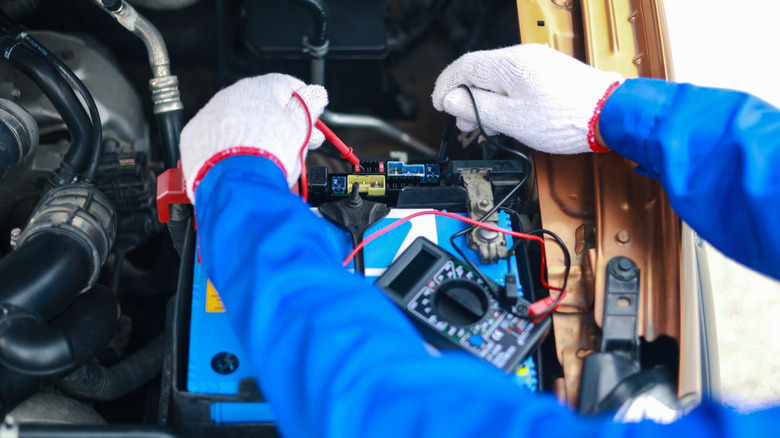 A mechanic wearing gloves using a multimeter to test out car's fuses.