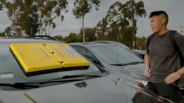 A young driver is disappointed to find a parking barnacle on their windshield