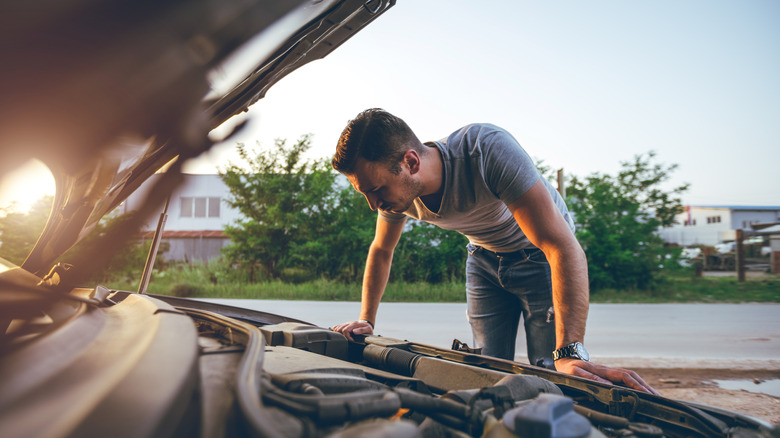 A man looking at his car's engine with an open hood