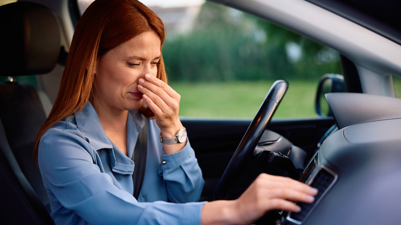 A woman holding her nose while adjusting an AC vent
