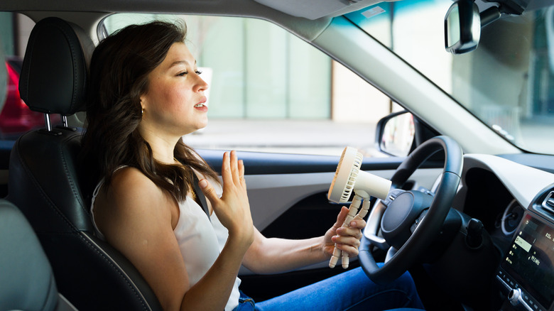 A woman using a handheld fan in her car to keep her cool