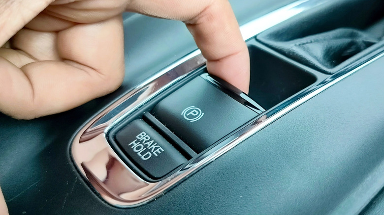 A person's finger engaging the electronic parking brake on a car