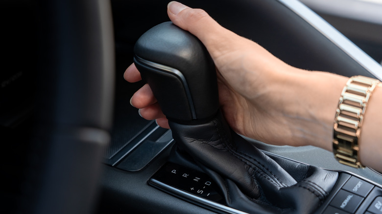 A hand with gold watchband shifts an automatic transmission into park