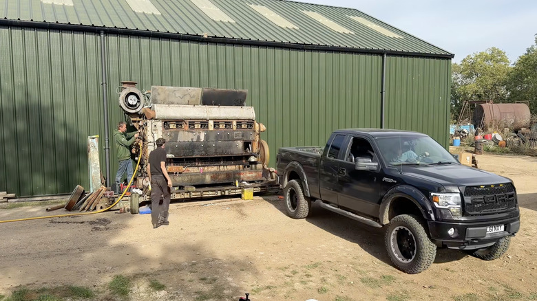 A 102.4-liter Mirrless generator engine about to be jump-started by a Ford F-Series pickup truck.
