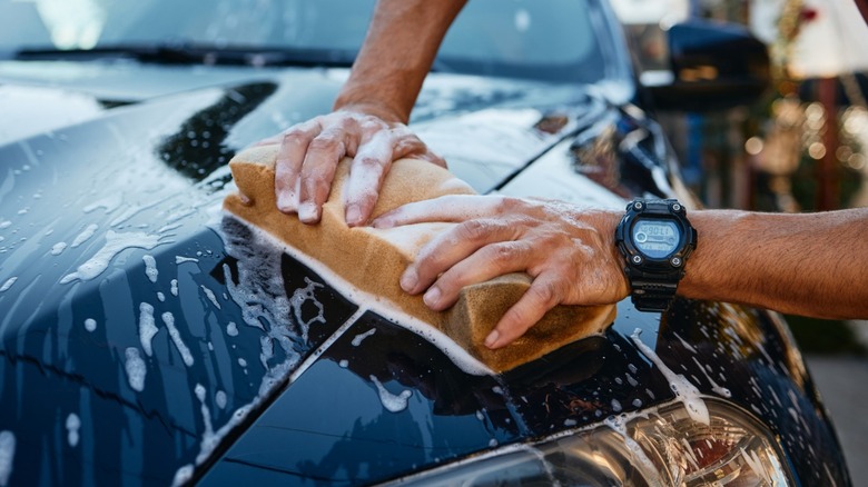 A person hand washing a dark-painted car with a sponge