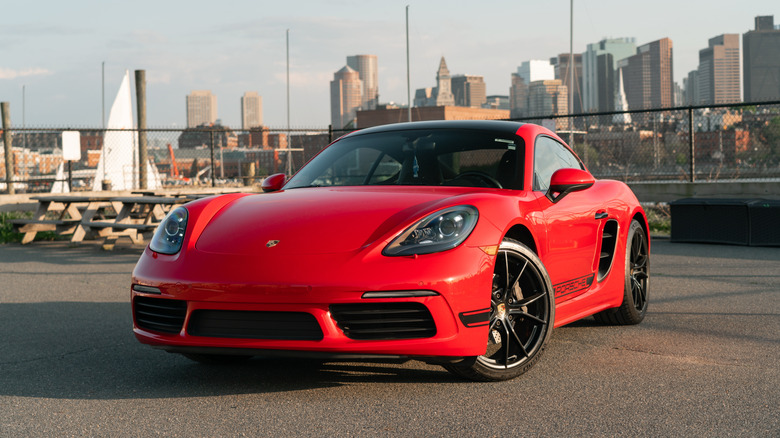 A red Porsche 718 Cayman parked at a marina